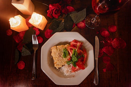 Assiette de gratin avec tomates et herbes, décorée de pétales de rose et bougies, ambiance romantique.