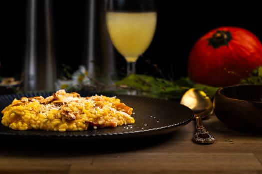Risotto crémeux à la courge, garni d'amandes, avec un verre de boisson et une décoration automnale en arrière-plan.