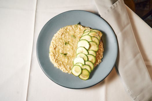 Risotto crémeux au coco garni de tranches de courgette sur une assiette bleue, servie sur une nappe blanche.